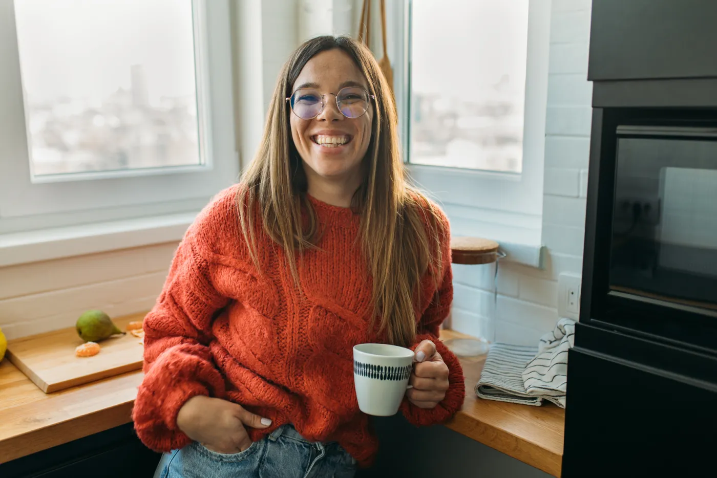 A coach smiling with a cup of coffee in her kitchen