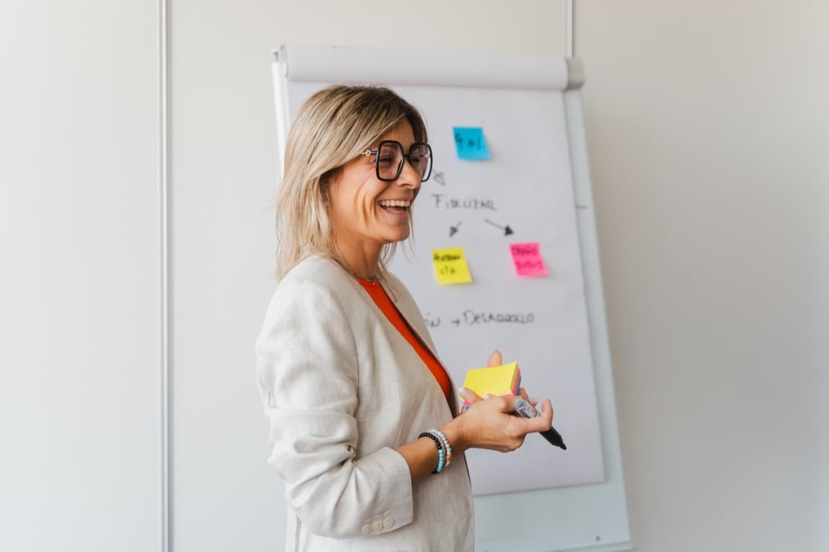 Leadership coach smiling while facilitating a whiteboard planning session